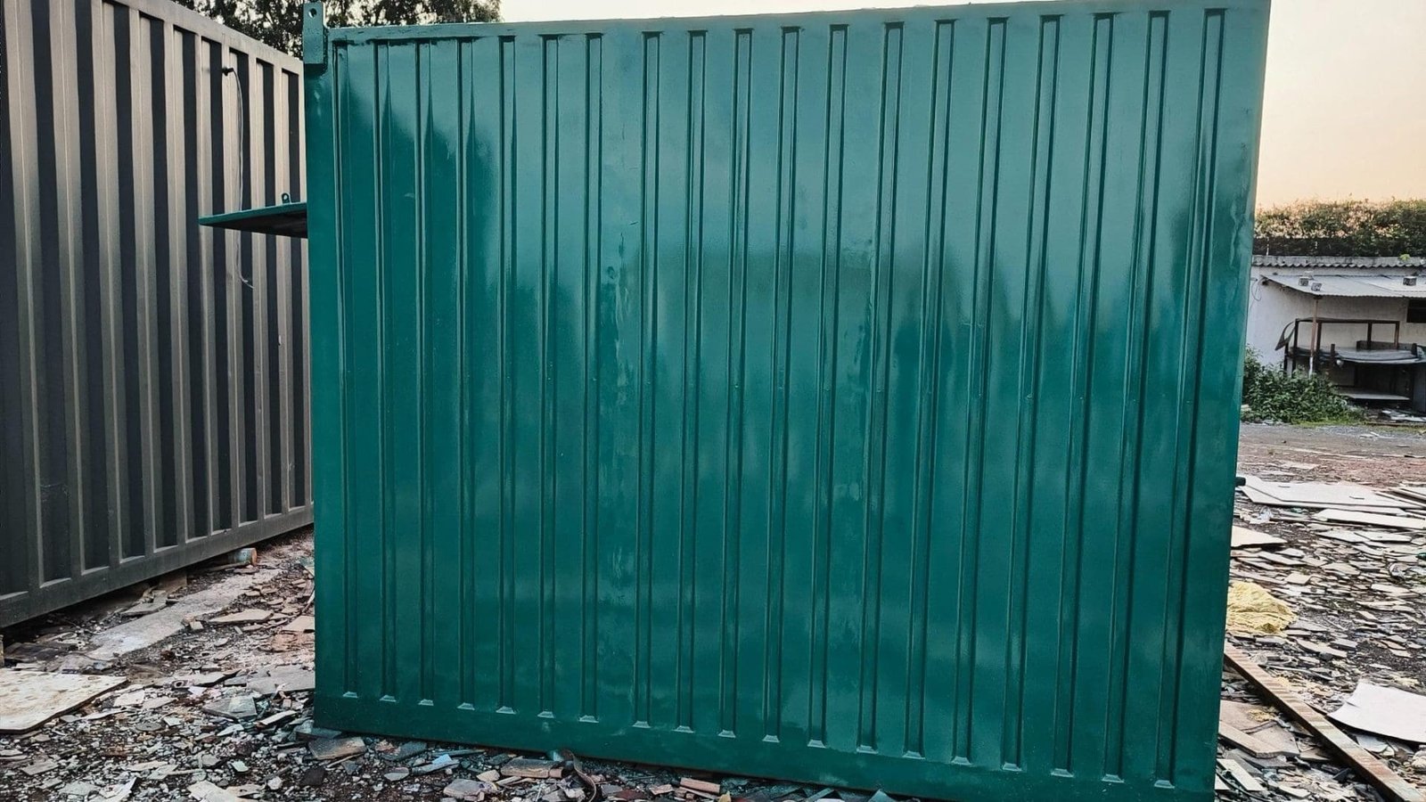 Green portable cabin with a plain wall on a construction site.