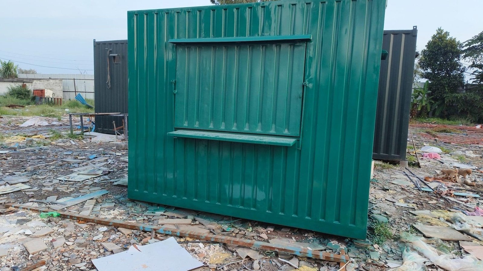 Green portable cabin with a service window on a construction site.