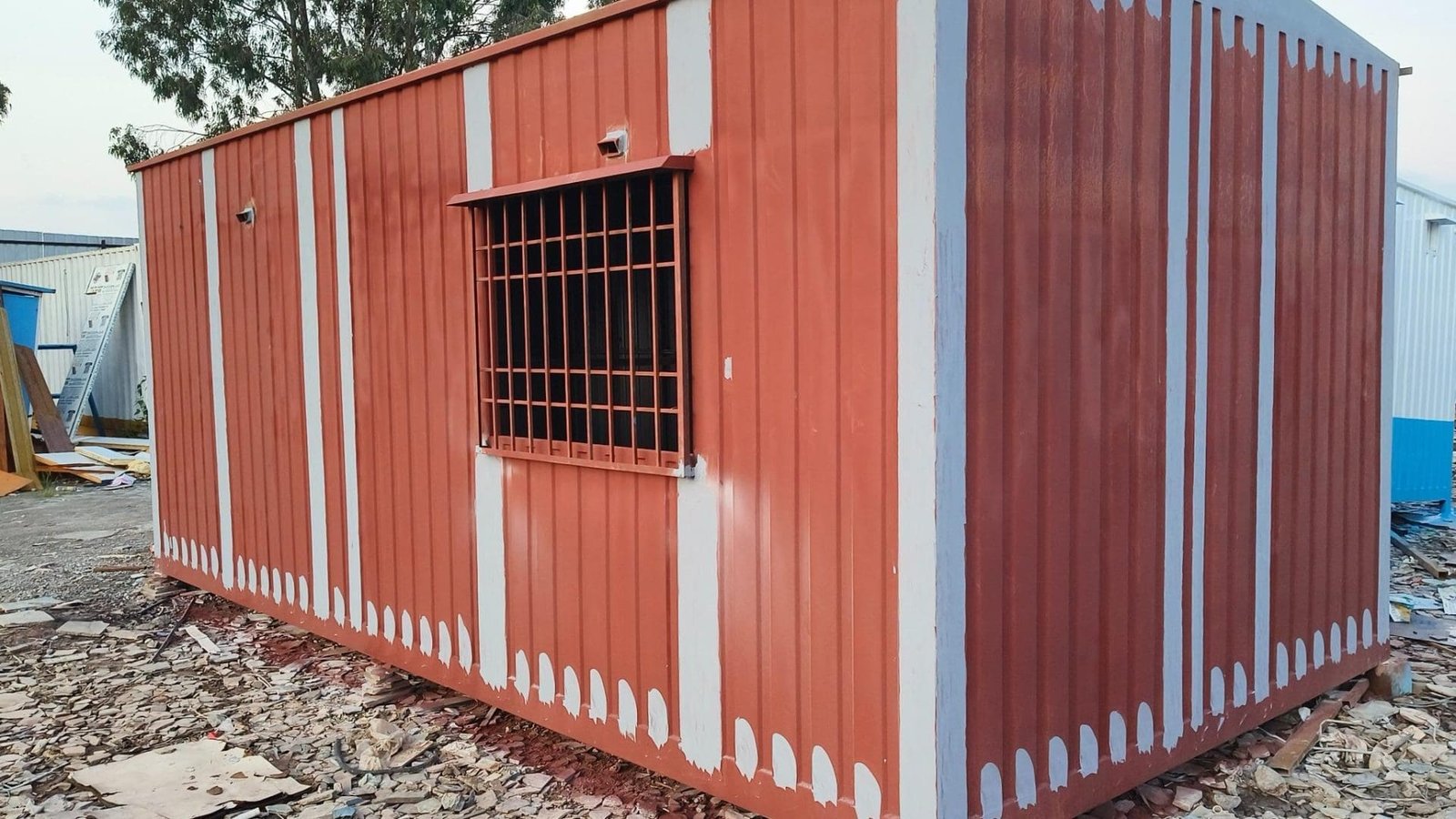 Red portable cabin with white stripes, situated on a construction site.