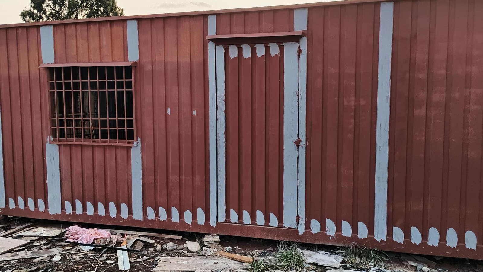 Red portable cabin with white stripes, situated on a construction site.